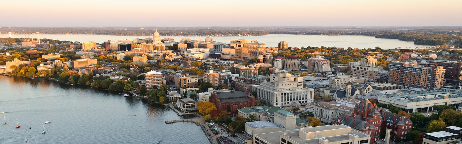 A wide shot of the Isthmus with the capitol building at the center. You can see the lakes on the bottom left and top right corners with a slight hint of morning daylight.