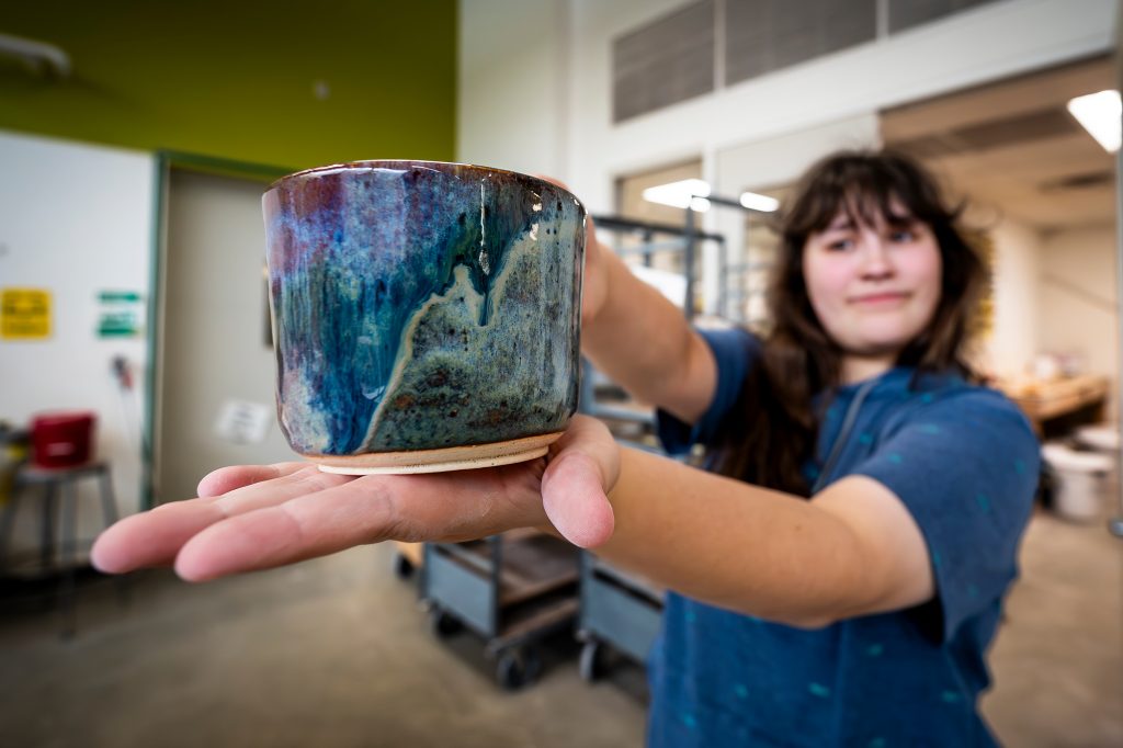 Person holding a ceramic cup with a multicolored glaze in a workshop setting.
