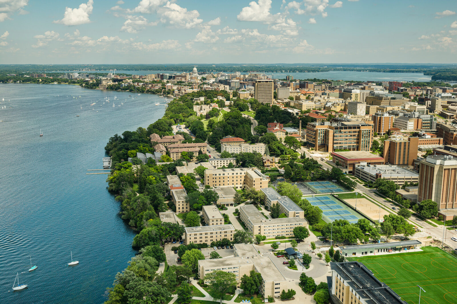 The Cole Beach and Lakeshore Tennis Courts and the Lakeshore neighborhood are photographed  by a drone with the Capitol and the campus skyline on a partly cloudy summer day at the University of Wisconsin–Madison on July 2, 2025. Lake Mendota (left) and Lake Monona (right) frame the isthmus.