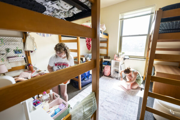 Two students work to decorate their respective spaces in a shared residence hall room.